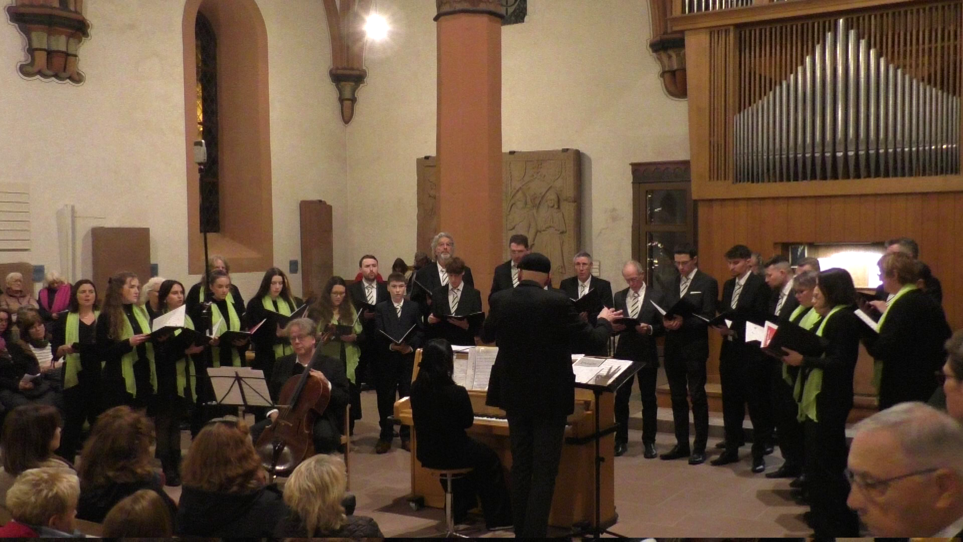 Ein gemischter Chor singt in der evangelischen Kirche in Schönau. Der Dirigent steht dabei neben einem Klavier, die Pianistin begleitet den Chor. 