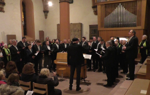 Ein Männerchor singt in der evangelischen Kirche in Schönau. Der Dirigent steht dabei neben einem Klavier.